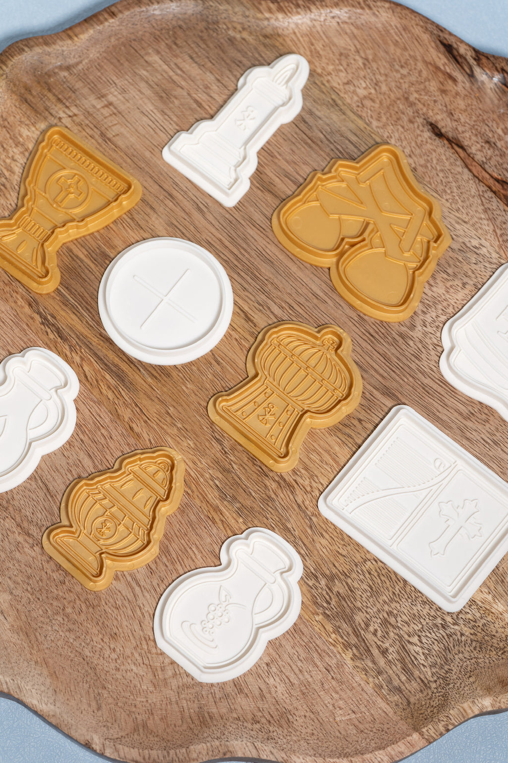 A set of plastic play dough molds of items used during a catholic mass. these items include a candle, bells, chalice, host, ciborium, missal, thurible and wine decanter displayed on a wooden plate. 