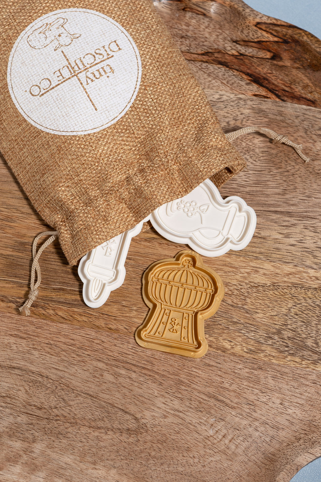 A small drawstring bag with the words tiny disciple co on it showing a ciborium, wine decanter and candle spilling out of the bag.
