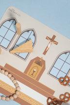 A close-up of a silicone mat with an image of a Catholic Church altar table. This table has wooden pieces, including a triangular piece, a wooden cross, and a beaded bracelet, arranged on a light blue background.